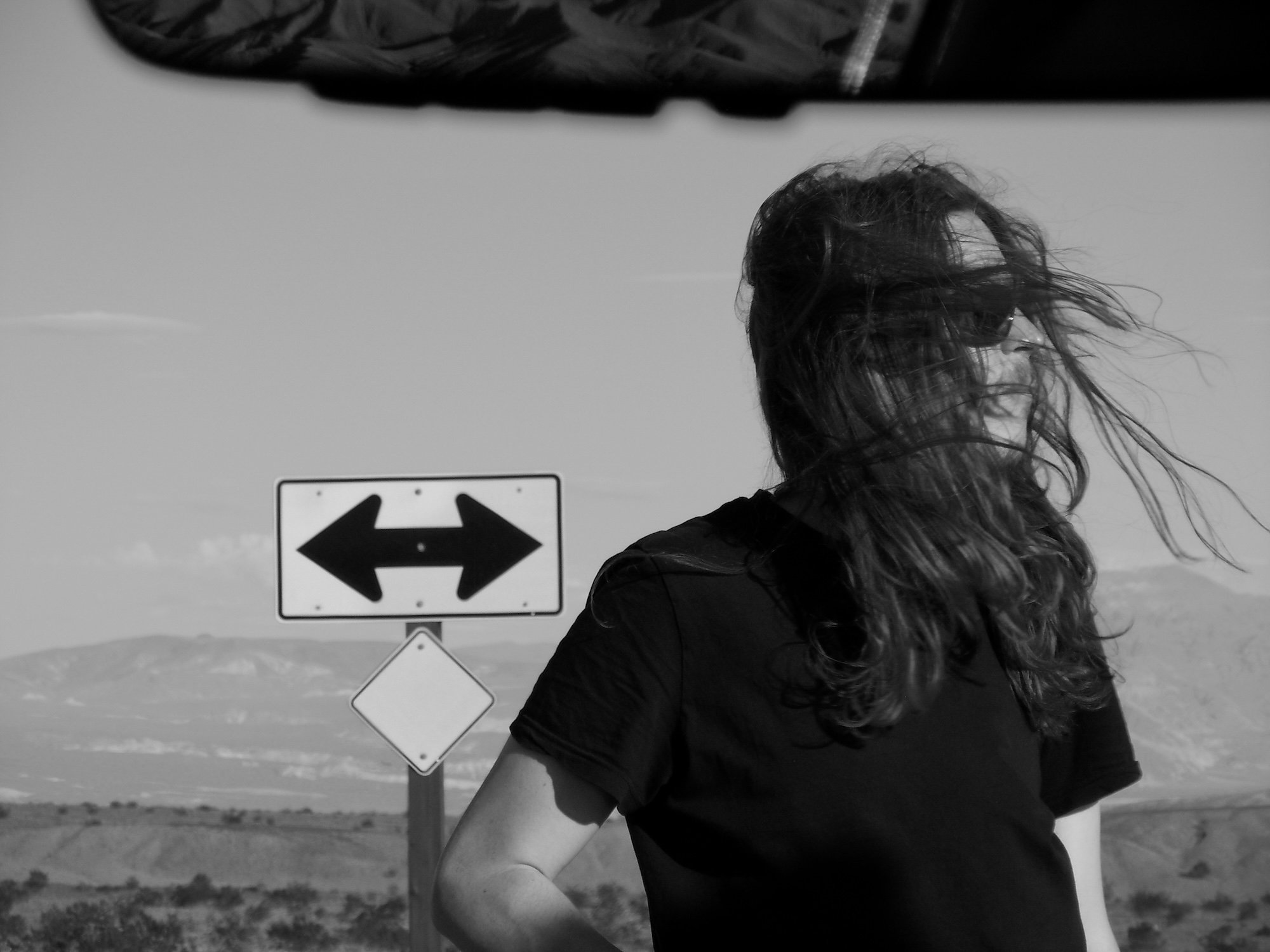 Person with long hair in wind, road sign behind